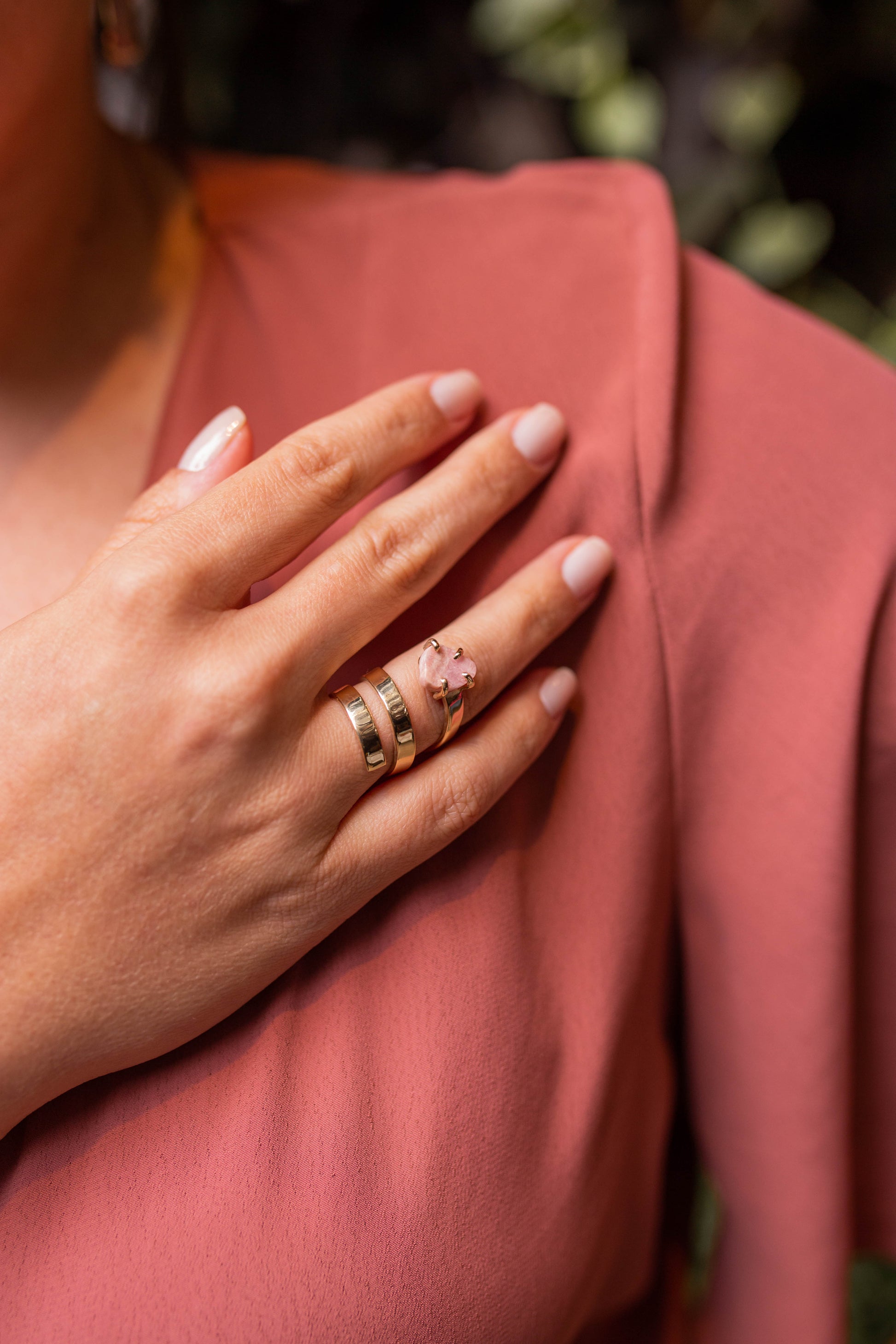 Mulher de camisa rosa com a mão no ombro usando o anel Ruta 40 em ouro 18k com pedra Rodocrosita.  
