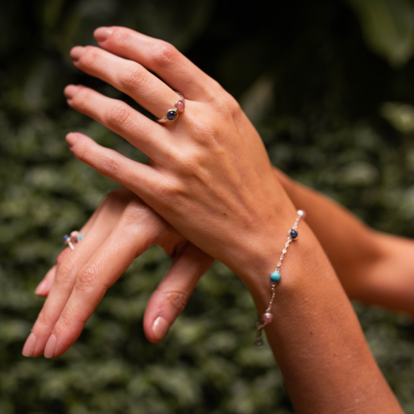 Mãos femininas com anéis e pulseira Cabo Horn com pedras Sodalita, Rodocrosita e Turquesa.